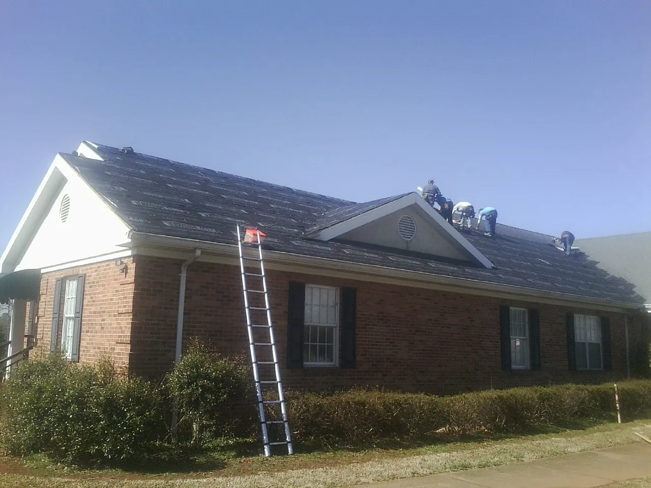 Crew tearing shingles off a brick ranch roof with a ladder set — Metal Roof Repair work by our crew in Laura