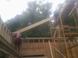 Carpenter raising a rafter beam on a new second story frame in Laura