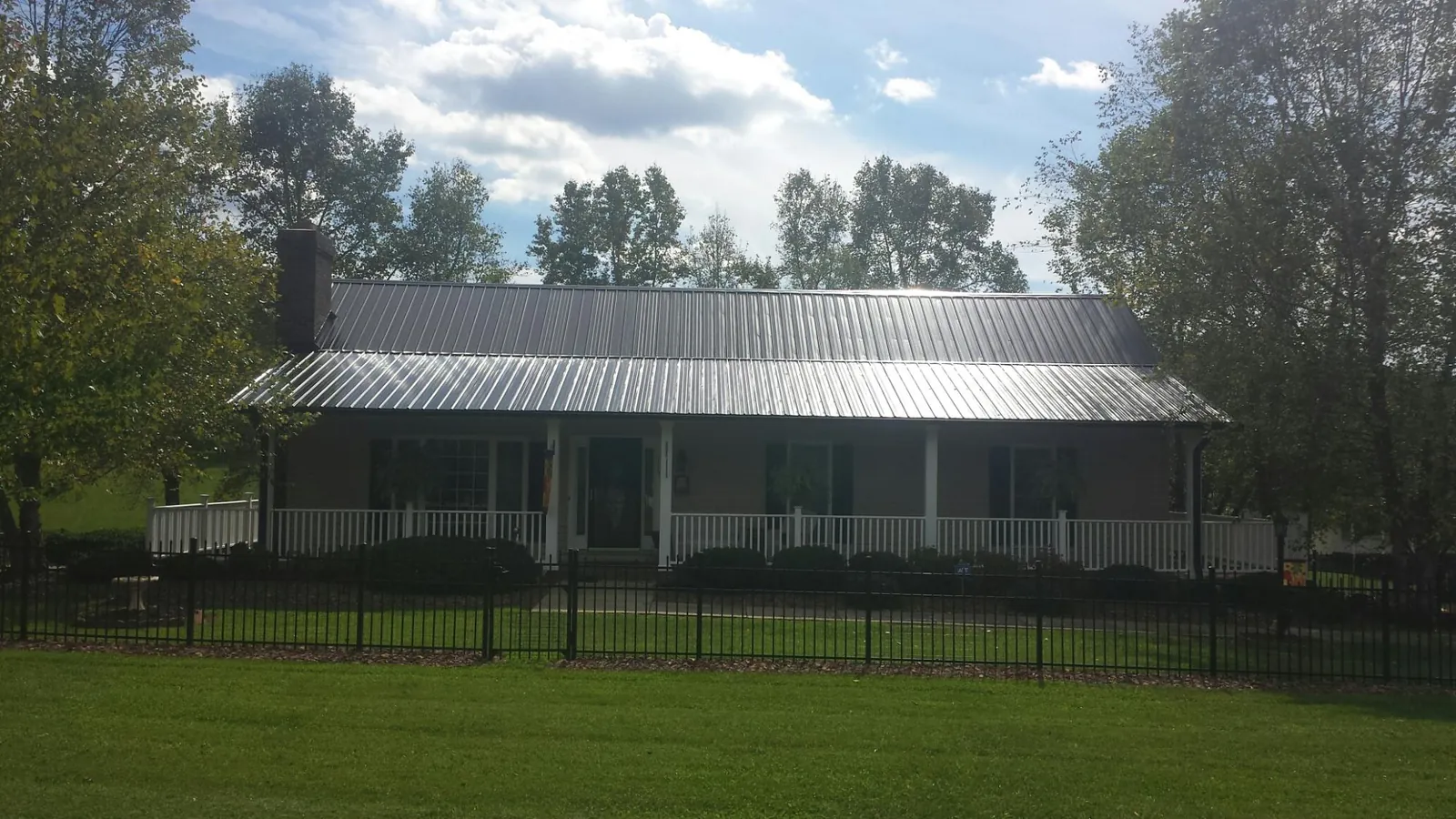 Gray metal roof on a brick ranch with a full width front porch — Gutter Guard Installation work by our crew in Laura